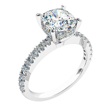 A platinum or white gold cushion cut diamond solitaire engagement ring with diamonds on the band and a hidden halo in a claw setting