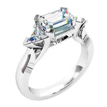 A platinum or white gold emerald cut diamond set horizontally trilogy solitaire engagement ring featuring two trilliant cut diamonds