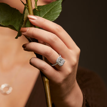 A woman wearing a radiant cut diamond cluster halo engagement ring whilst holding a rose