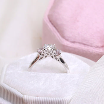 An 18ct white gold round brilliant cut diamond trilogy engagement ring featuring two argyle certified natural pink diamonds