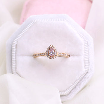 An 18ct rose gold pear shaped pink argyle diamond halo engagement ring with diamonds on the band in a claw setting